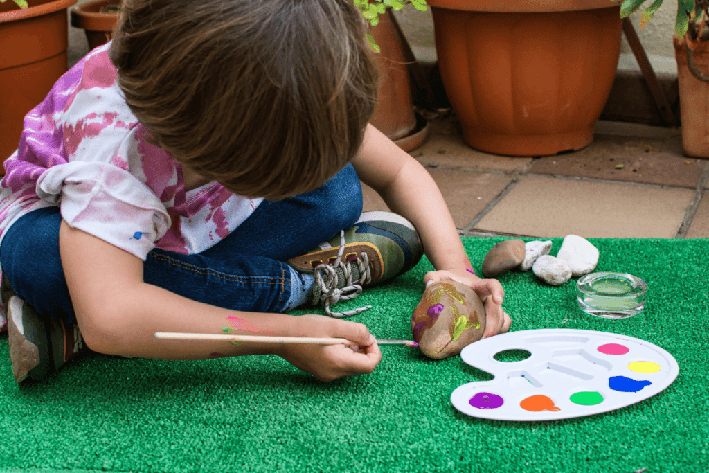 child painting a rock outside 